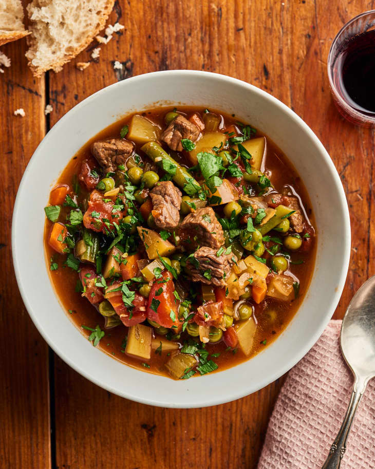 beef stew sits finished in a bowl with cheese and a spoon on a napkin near it