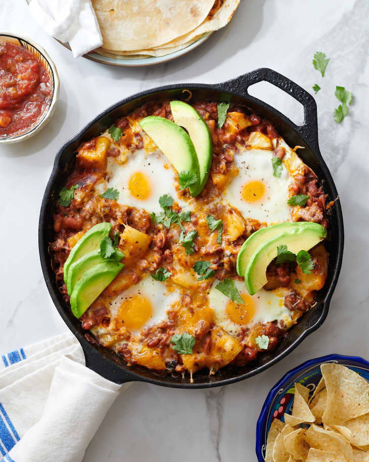 breakfast skillet sits in cast iron pan with handle wrapped in towel with avocado garnish
