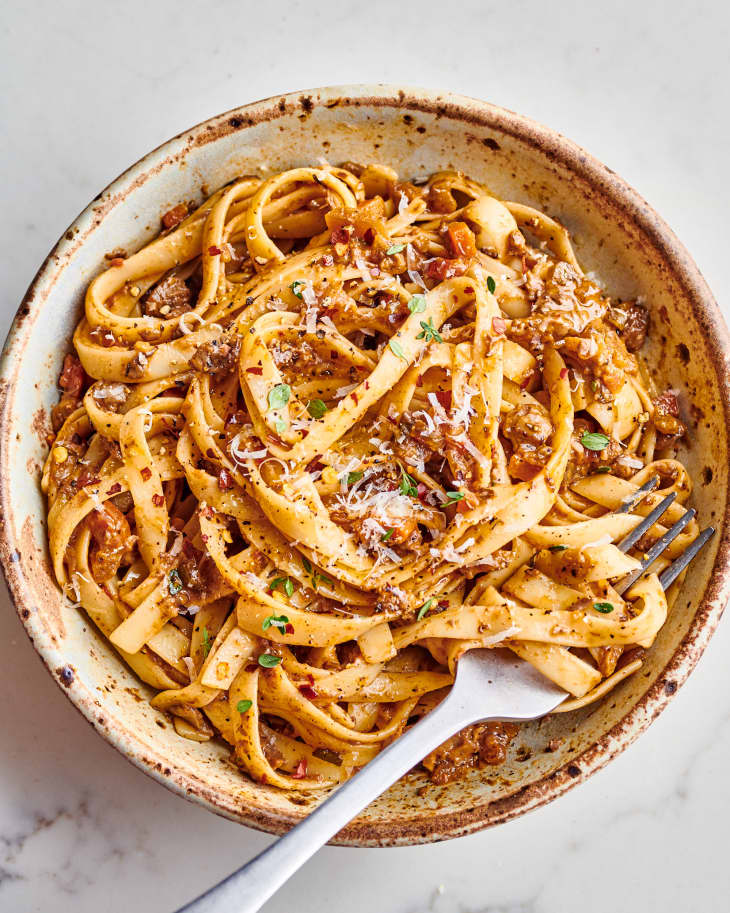 mushroom bolognese fettuccini is in a bowl, garnished with parmesan cheese and a fork in it