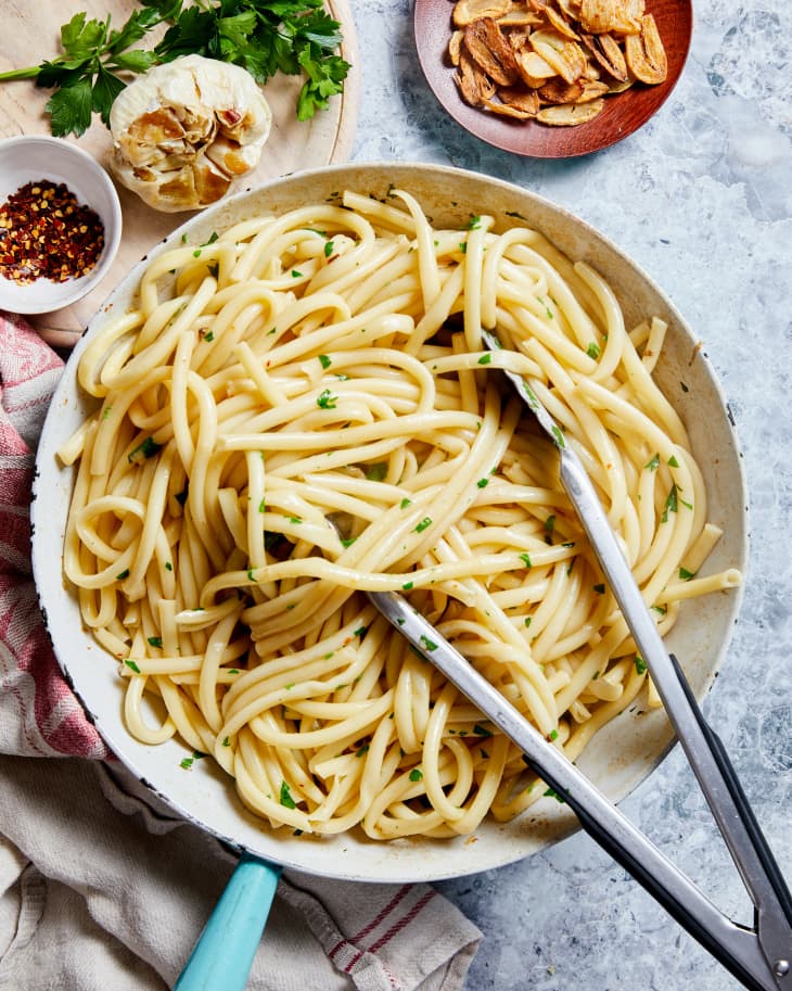 garlic pasta sits in a pan on the table with tongs resting in it