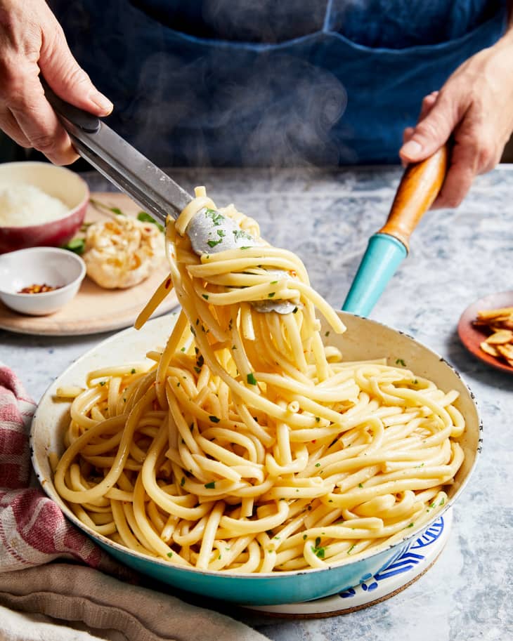 someone is stirring pasta in a pan with tongs