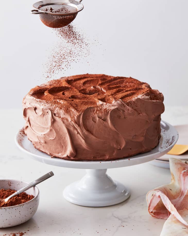 someone is sprinkling cocoa powder on the cake on a cake stand