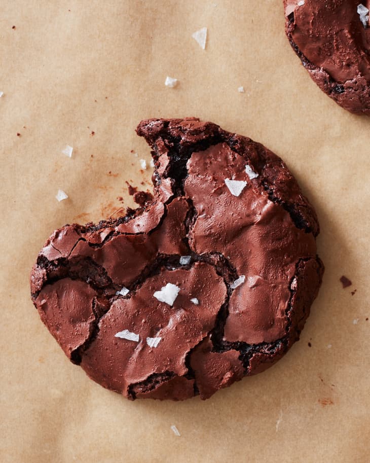flourless chocolate brownie cookies sit on a sheet of parchment paper with a bite taken out