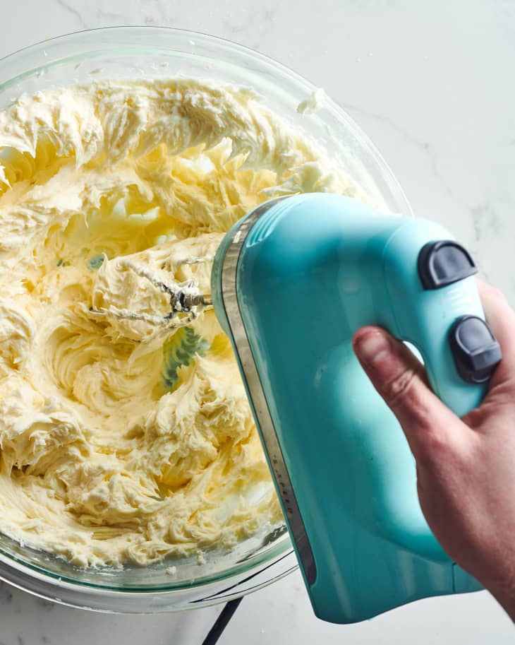 Someone using a hand mixer to mix cheesecake batter