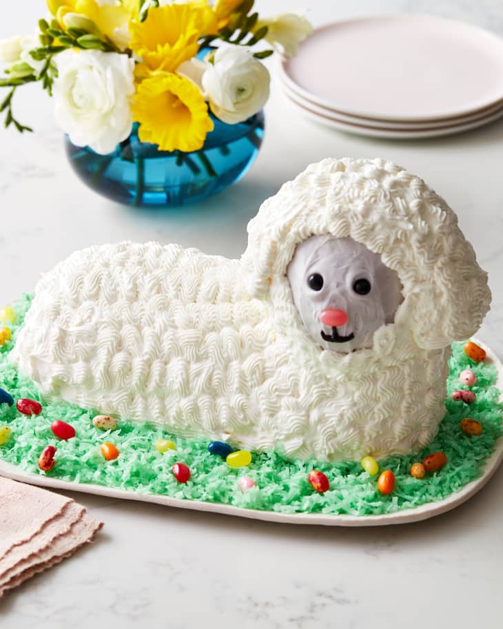 lamb cake sits on green icing in front of plates and flowers
