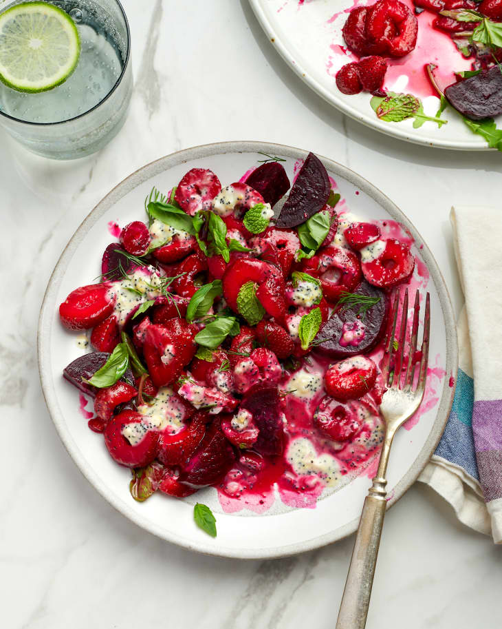 beet and strawberry salad on a plate next to cutlery and water with lime