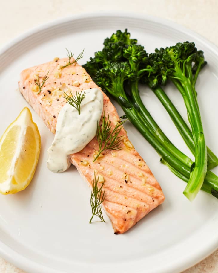 lemon salmon with dill garnish on a plate next to broccolini