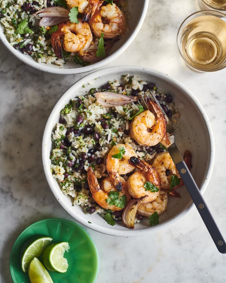 broiled shrimp on top of cilantro rice in a bowl next to lime wedges