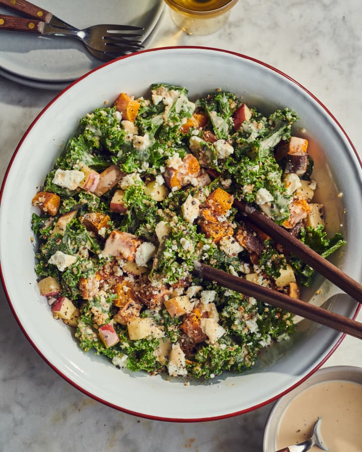 Kale and quinoa salad in large white bowl with serving utensils inside the bowl