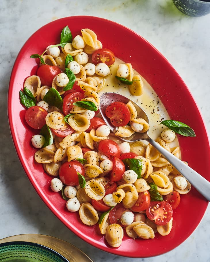 caprese pasta salad in a red dish with a metal spoon in it