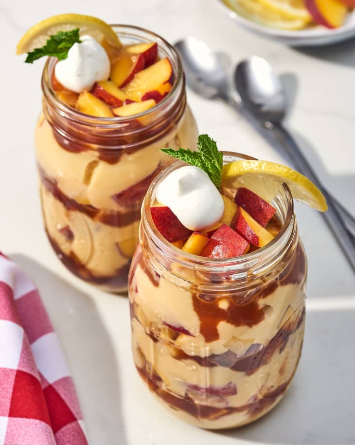 two mason jars of peach iced tea trifle next to each other on a table with spoons and a red napkin