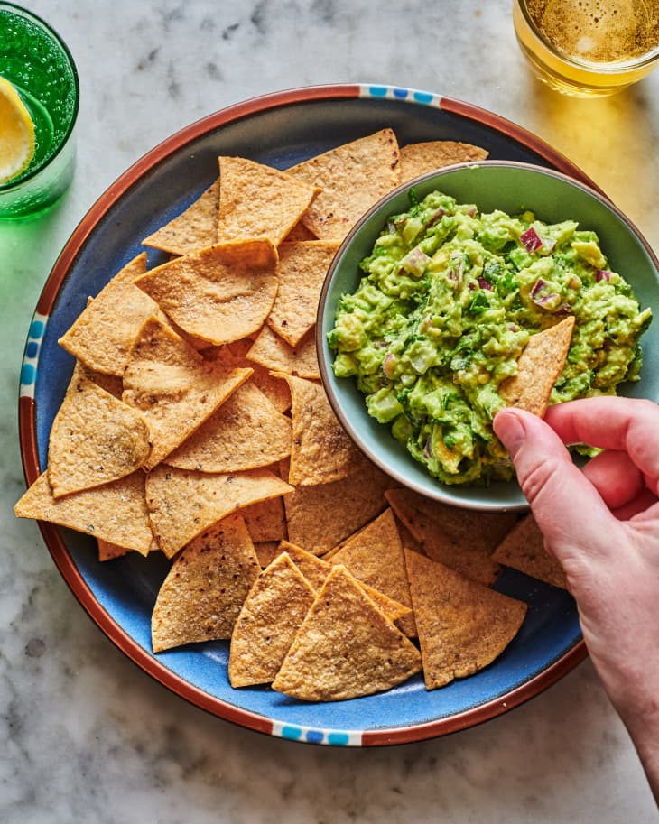 A platter of tortilla chips, with a hand dipping one in guacamole