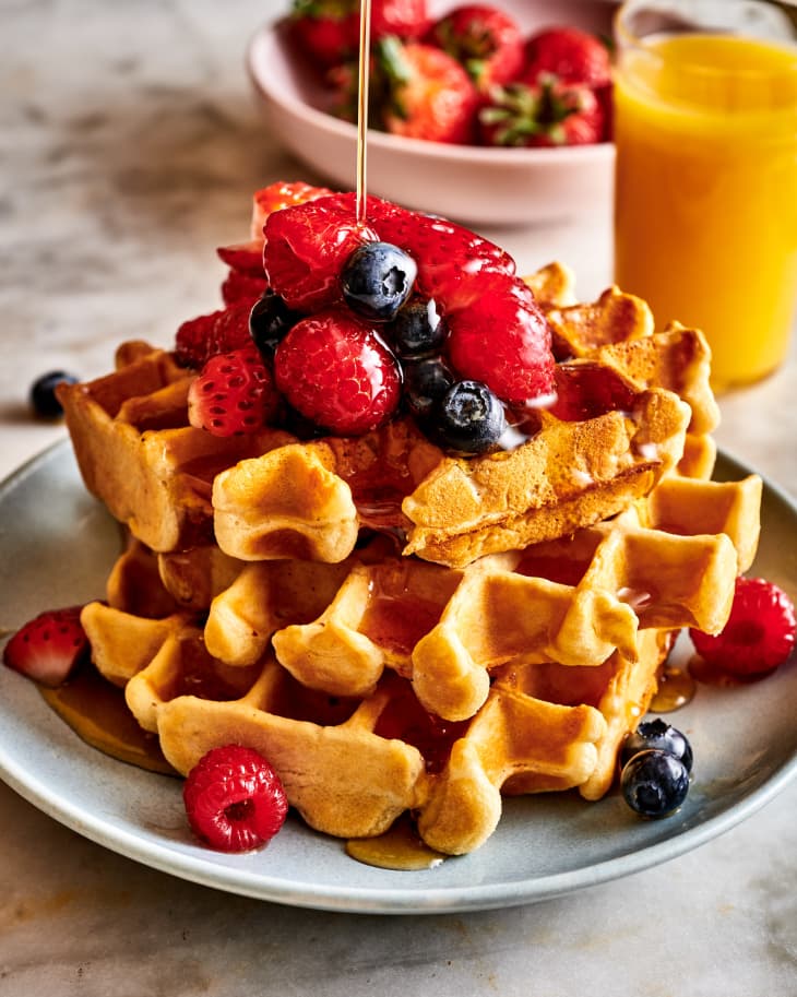 vegan waffles, garnished with berries, being drizzled with maple syrup