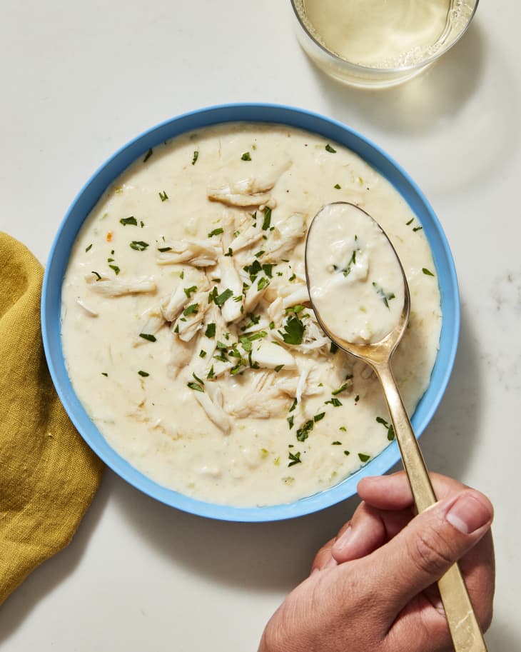 she crab soup in bowl with hand taking gold spoon out