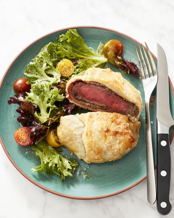 Individual beef wellington sliced open on plate. Served with side salad.