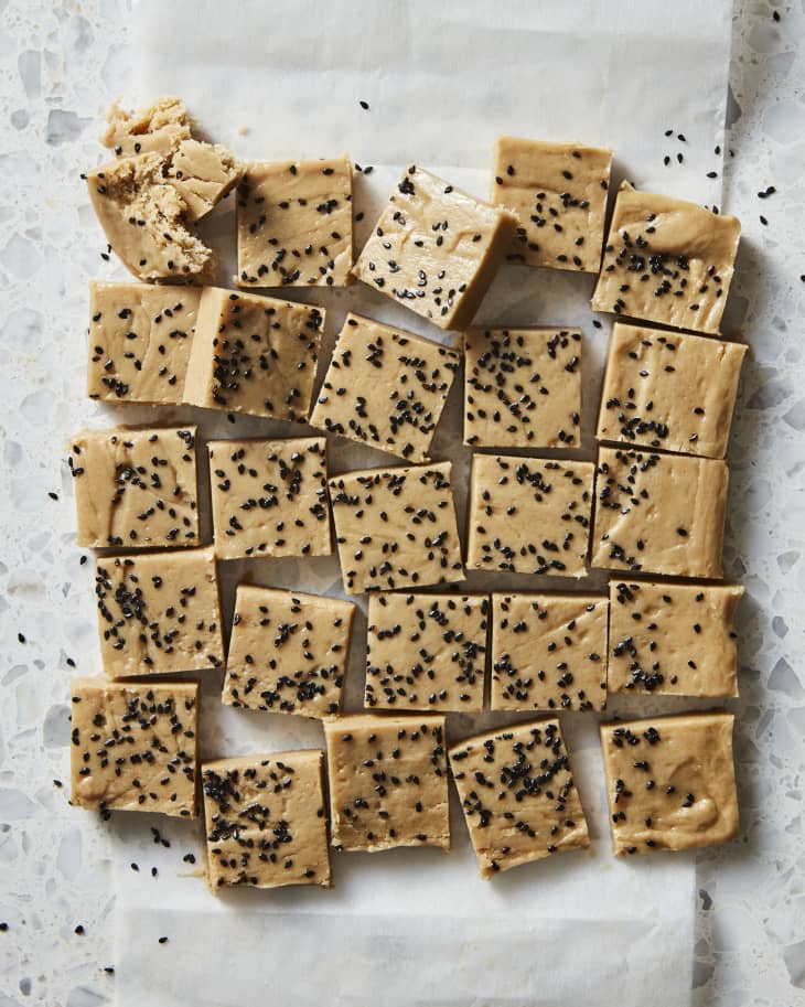 Overhead photo of squares of homemade halva on white parchment, one broken to show texture