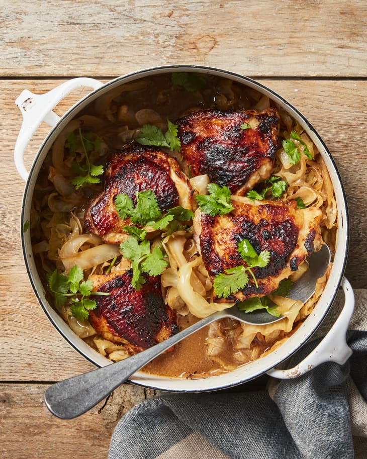 Overhead photo of one-pan-miso butter chicken and cabbage garnished with cilantro in dutch oven on wood surface.