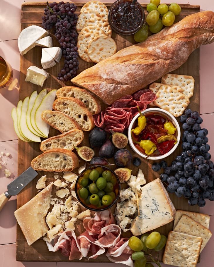 antipasto on wood board: sliced bread, olives, grapes, cheese, peppers, crackers, cured meat