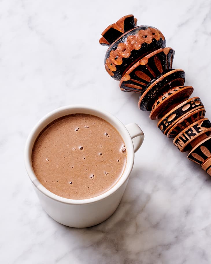 Champurrado in mug on surface with a molinillo beside.