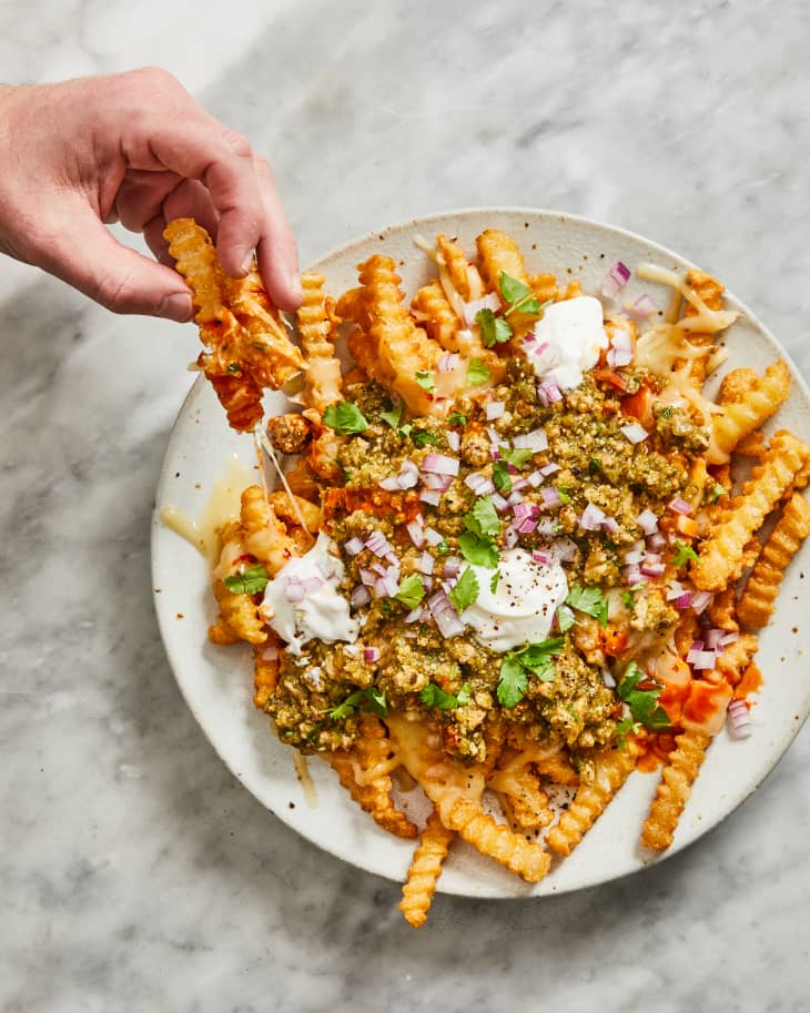 someone taking a chili cheese fry from a plate