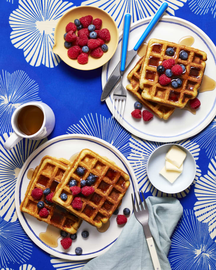 Brown sugar cornmeal waffles topped with fresh berries and syrup on colorful surface.