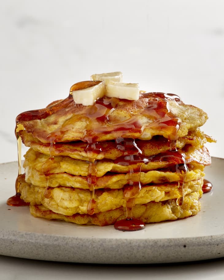 stack of pancakes on a plate with bananas on top with maple syrup drizzling down