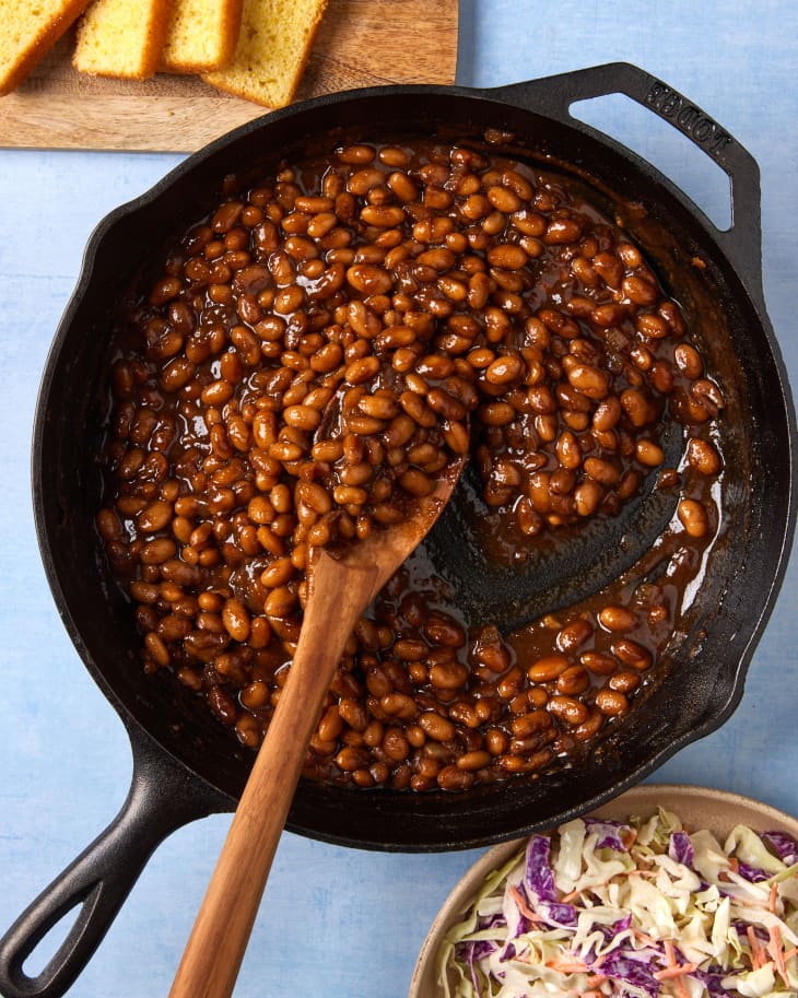 someone moving beans in a cast iron pan with a wooden spoon