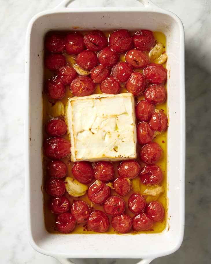baking dish with baked block of feta cheese, tomatoes, and garlic in olive oil