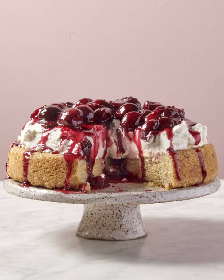 a shortbread cake topped with whipped cream and syrupy cherries with a slice taken out