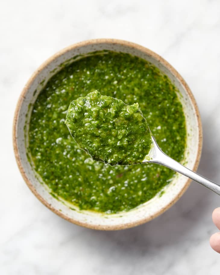 green chimichurri sauce on a spoon held above a bowl of chimichurri sauce on a marble surface