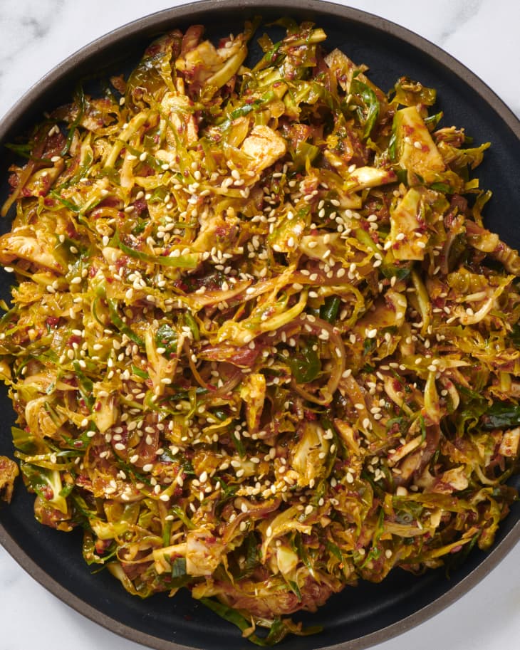 Brussels sprout kimchi on a black plate topped with sesame seeds