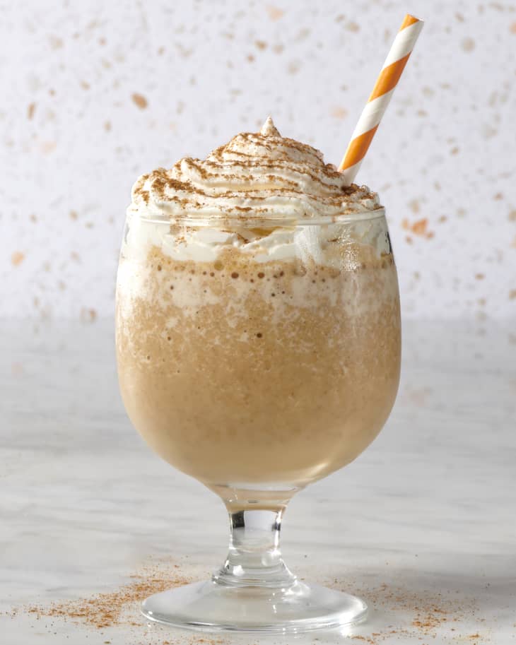 pumpkin spice latte in glass in front of tile with straw in it
