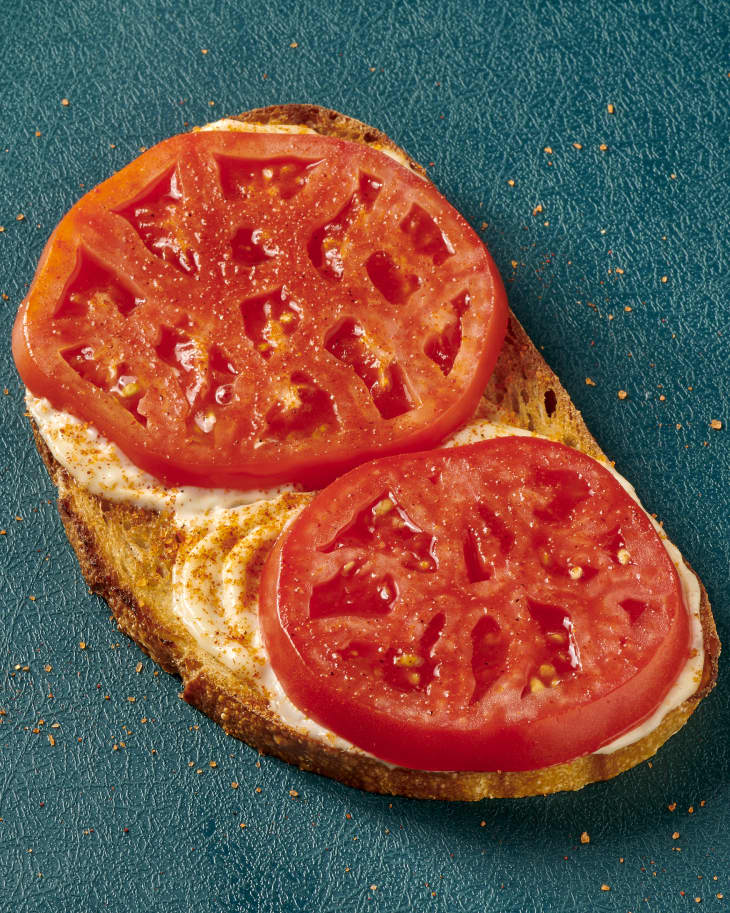 photo of tomato toast with mayonnaise, sliced tomatoes, and smoked salt on a blue cutting board