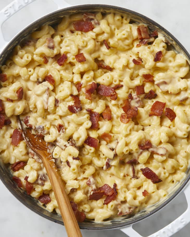 Overhead view of bacon mac and cheese in a white pot with a wooden spoon resting in it.