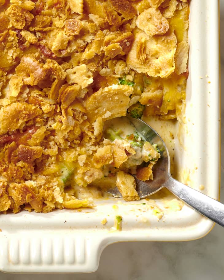 Close up view of broccoli and cheese casserole in a white square casserole dish with a spoon resting in the bottom right corner.