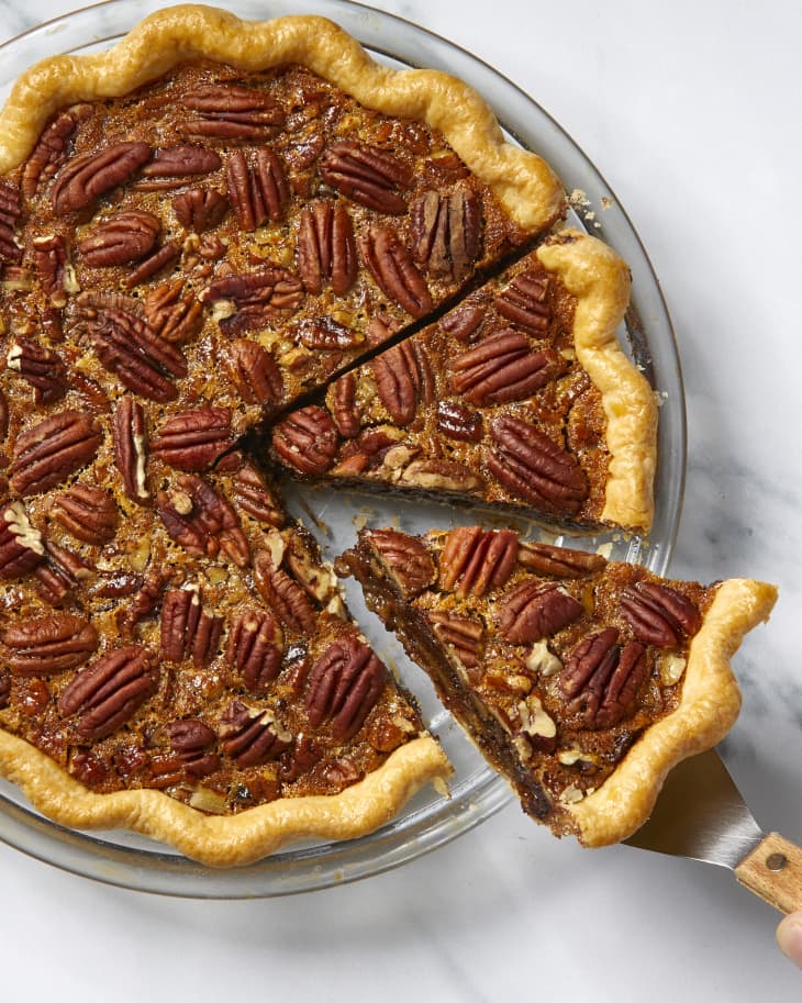 Overhead view of a slice of pecan pie being taken out of a whole pie in a glass dish.