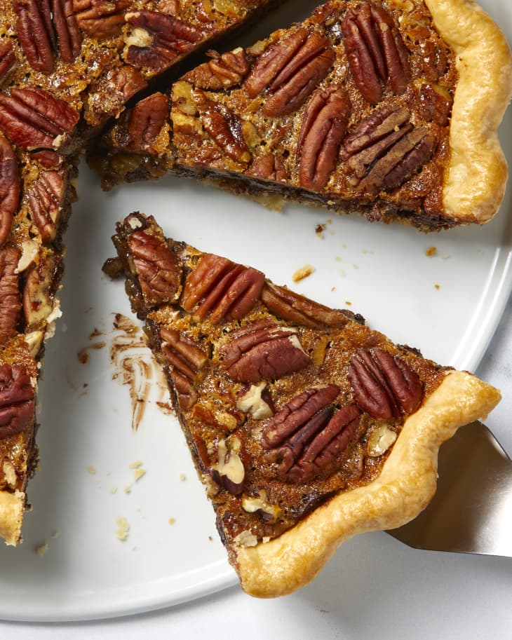 Overhead view of a slice of pecan pie being taken out of a whole pie on a white dish.