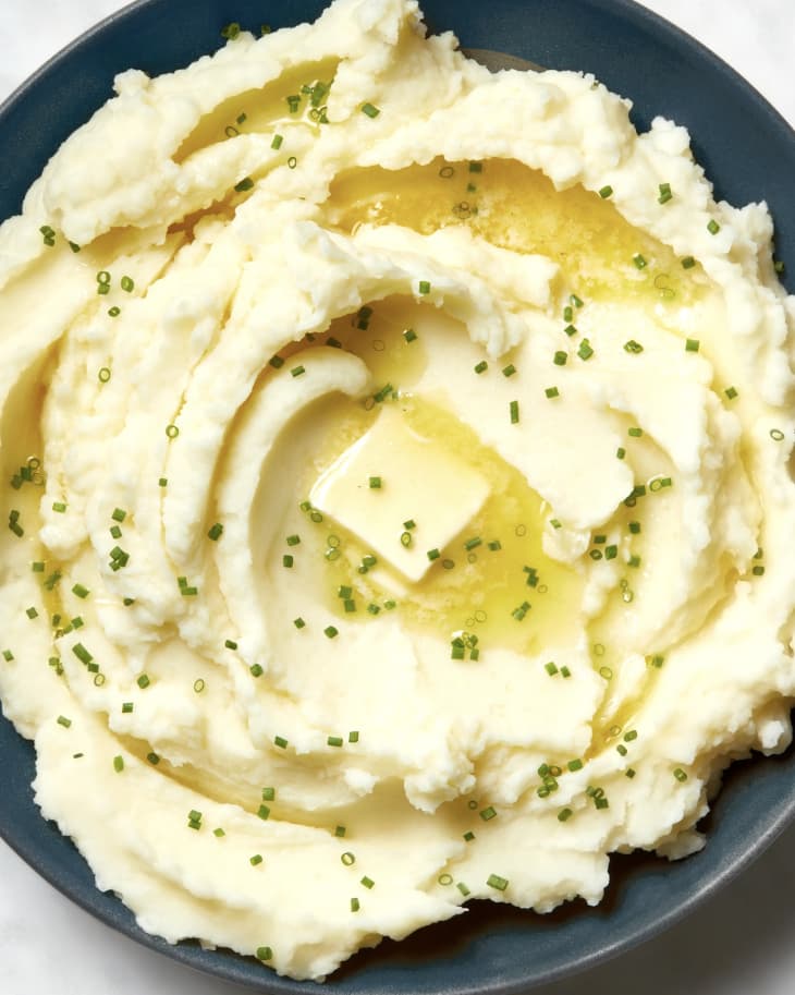 Overhead view of mashed potatoes in a grey bowl, topped with chives, a pat of butter and a spoon in the bowl.