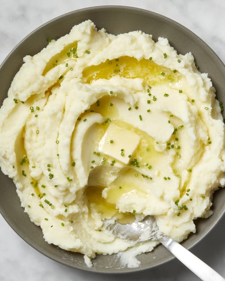Overhead view of mashed potatoes in a grey bowl, topped with chives and a pat of butter and a spoon in the bowl.