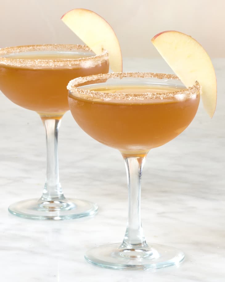 Two coupe glasses with harvest cocktail, cinnamon sugar rim and apple garnishes.