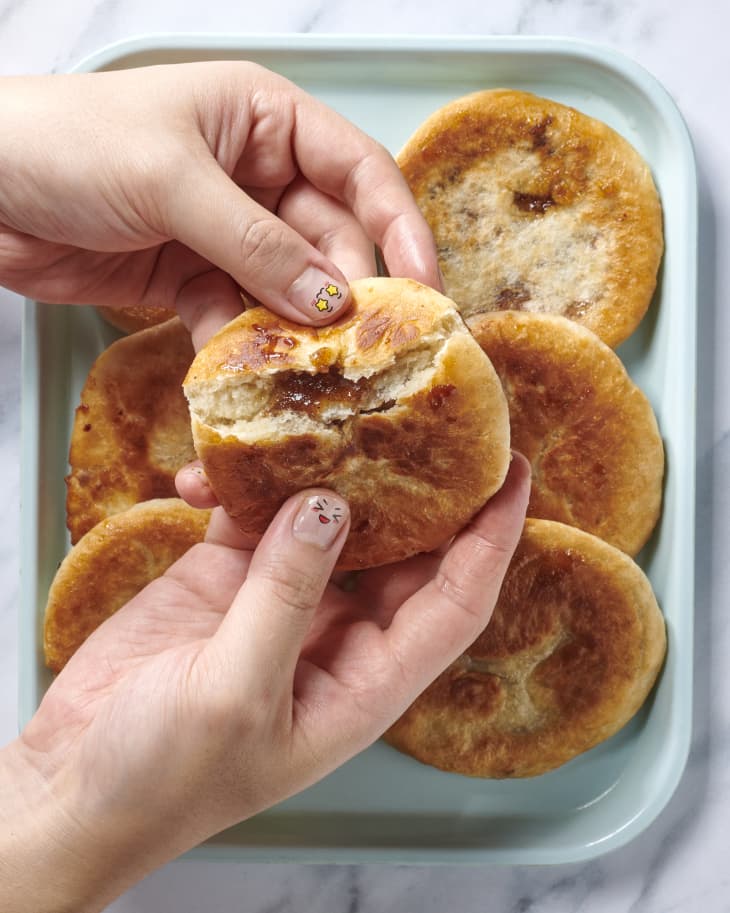 Overhead view of hotteok being pulled apart, showing the gooey inside, with a light blue plate of full hotteok below.