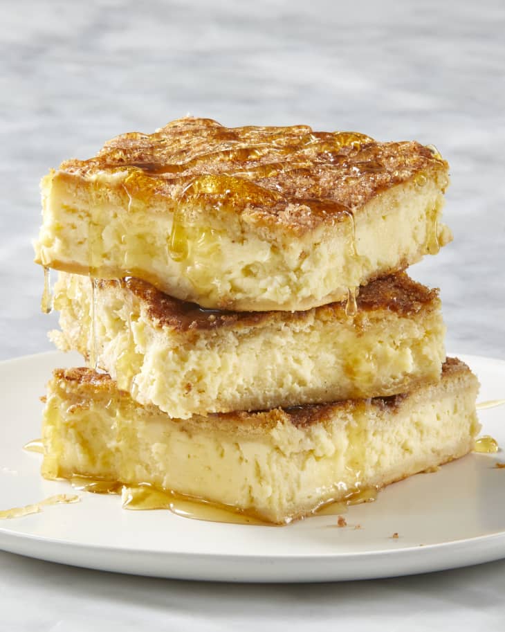 Front view of three pieces of cheesecake, stacked on each other on a white plate, drizzled with honey.