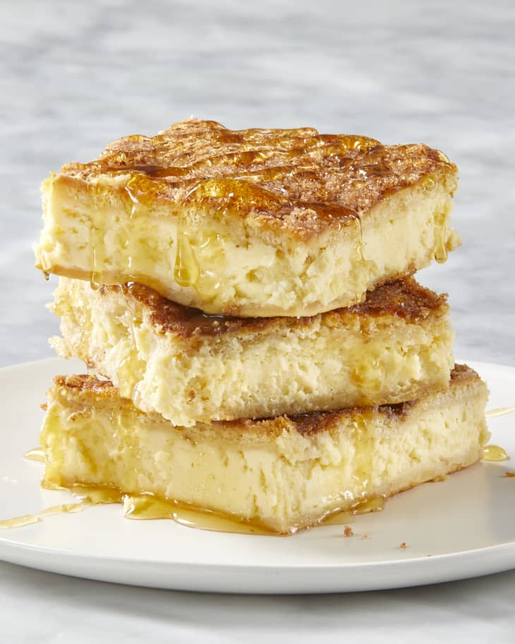 Front view of three pieces of cheesecake, stacked on each other on a white plate, drizzled with honey.