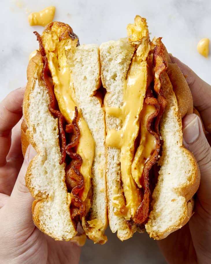 Overhead view of two hands holding open two halves of a bacon egg and cheese.