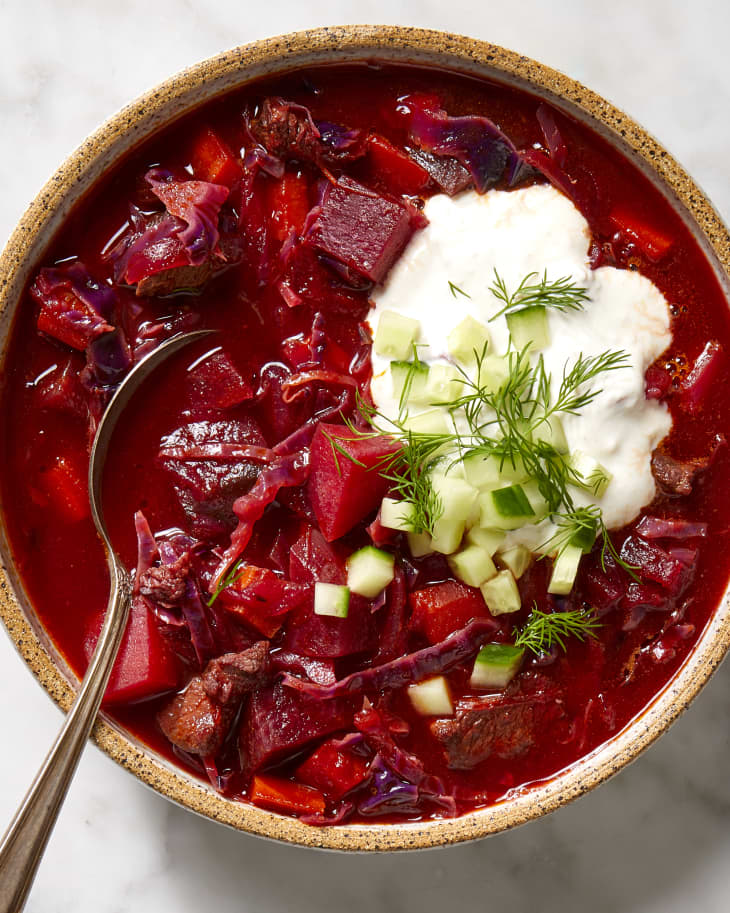Overhead view of borscht in a beige bowl, topped with sour cream, cucumber and dill.