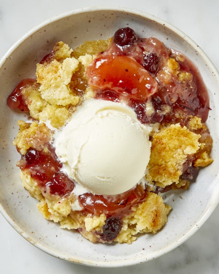 Overhead view of a serving of dump cake on a white speckled plate, with a scoop of ice cream on top.