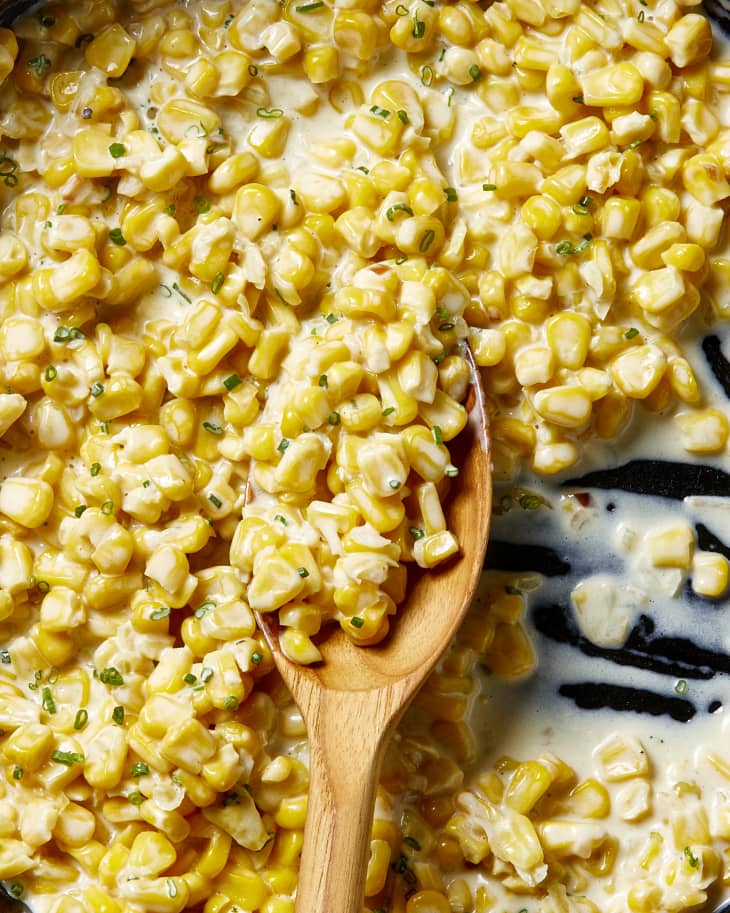 Overhead view of a wooden spoon resting in the creamed corn, with a scoop taken out of it.