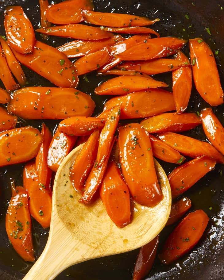Overhead view of glazed carrots in a pan with a wooden spoon.
