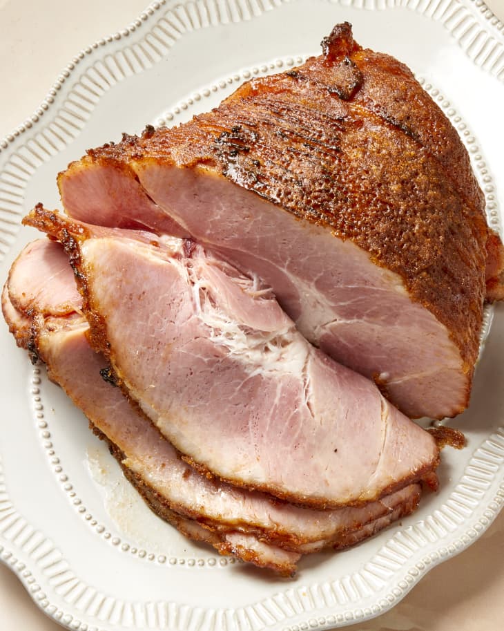 A sliced honey baked/glazed ham on an ornate platter on a warm color surface.