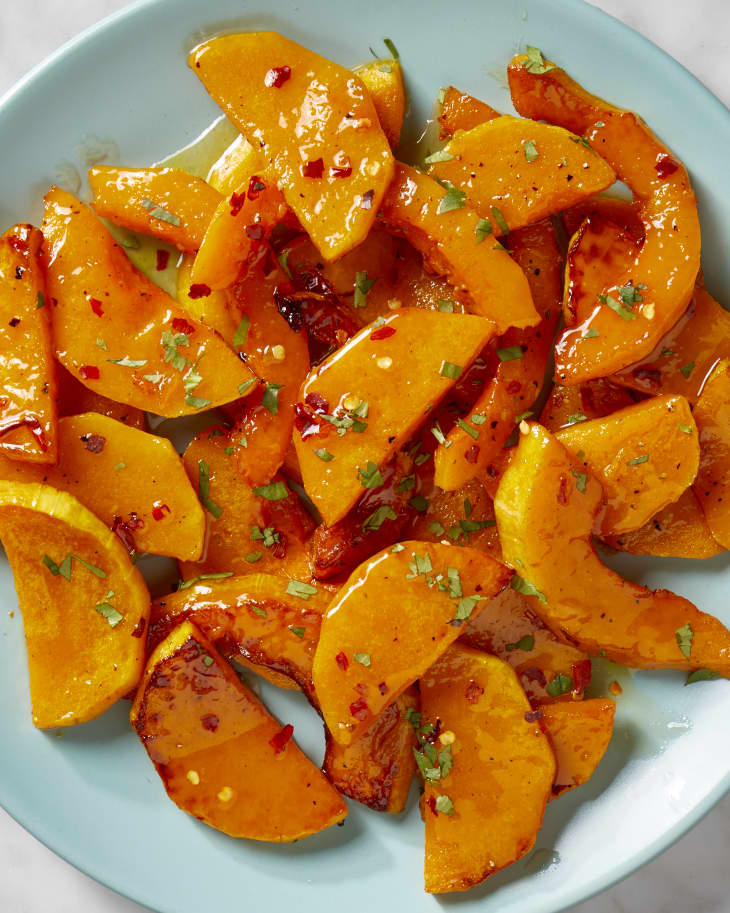 Overhead view of butternut squash on a light blue plate, topped with red pepper flakes and herbs.